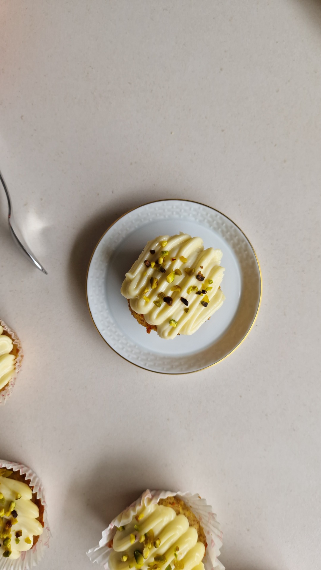 Cupcake mit cremigem Zuckerguss, bestreut mit Pistazien und Schokostückchen, auf weißem Teller.